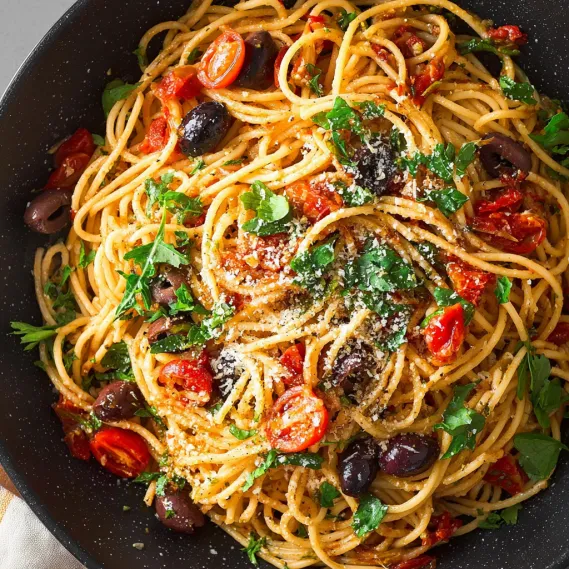 A bowl of pasta puttanesca with tomatoes, olives, and basil.