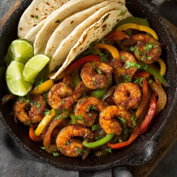 A plate of shrimp fajitas with a tortilla and peppers.