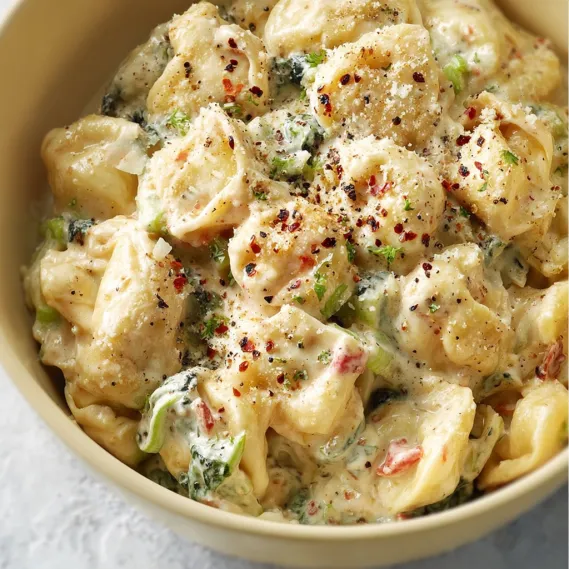 A bowl of creamy tortellini with vegetables.
