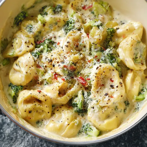 A bowl of creamy tortellini with broccoli and cheese.