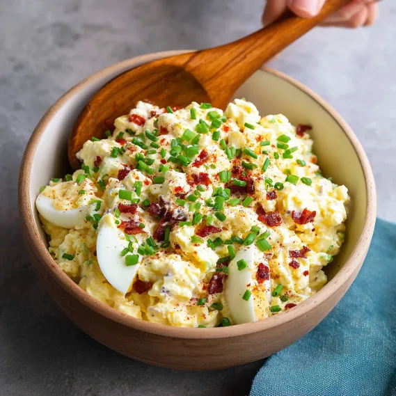 A wooden spoon is in a bowl of egg salad.