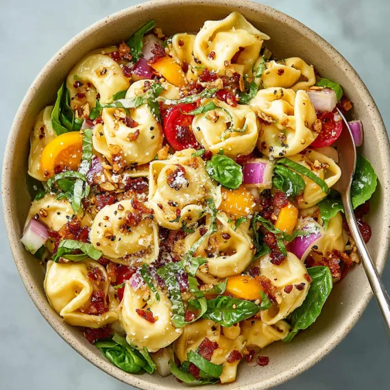A bowl of pasta salad with tomatoes, onions, and bacon.