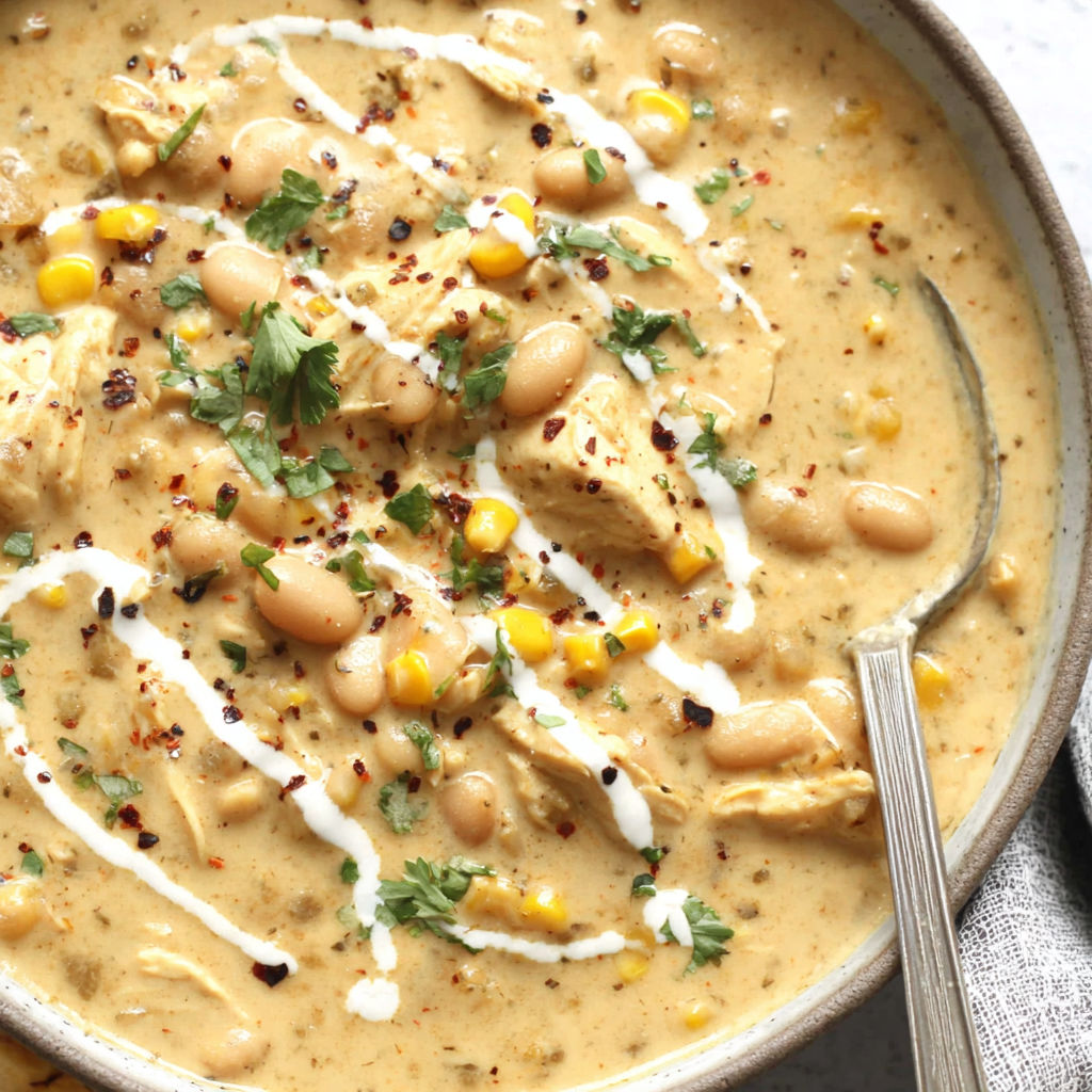 A bowl of soup with chicken, beans, corn, and white sauce.