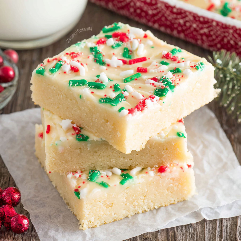 A stack of cake with white icing and green and red sprinkles.