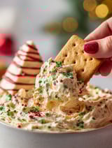 A person is dipping a cracker into a Christmas tree cake dip.