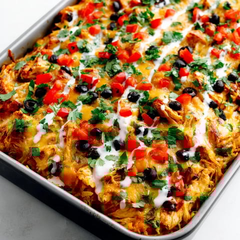 A pan of chicken burrito casserole with tomatoes, black olives, and cheese.