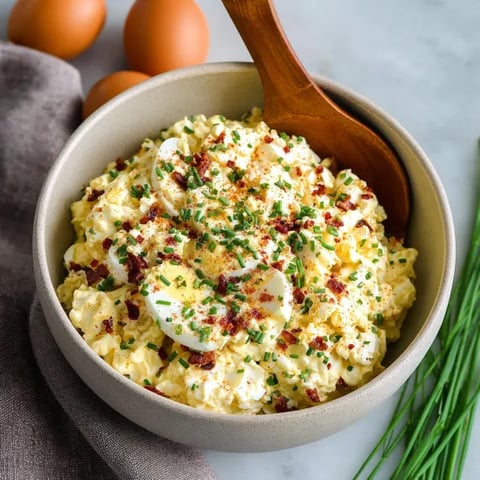 A bowl of egg salad with a spoon in it.