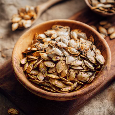 A wooden bowl filled with roasted pumpkin seeds.