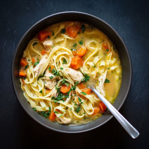 A bowl of chicken noodle soup with reames noodles.
