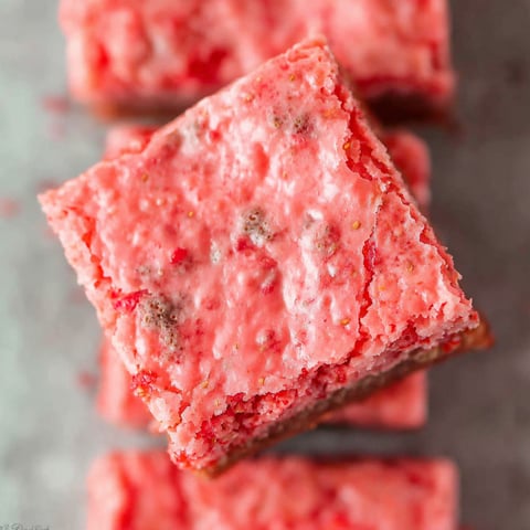A square of pink cake with red strawberries on top.