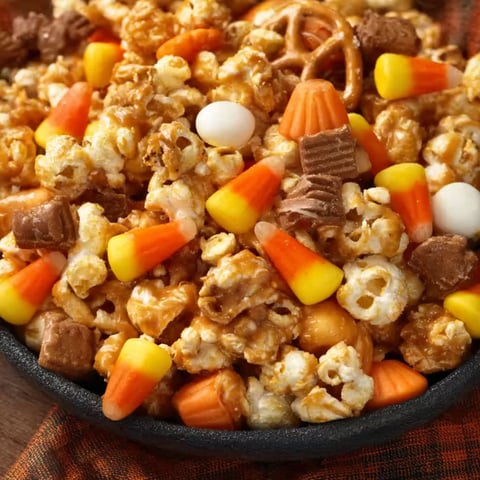 A bowl of popcorn with candy corn and other candy.