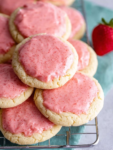 A stack of pink frosted cookies with a strawberry on top.